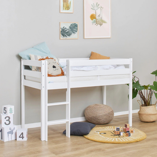White children's bed with toys and cushions in a room with framed pictures on the wall.